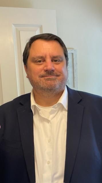 A man in a suit and white shirt is standing in front of a door.
