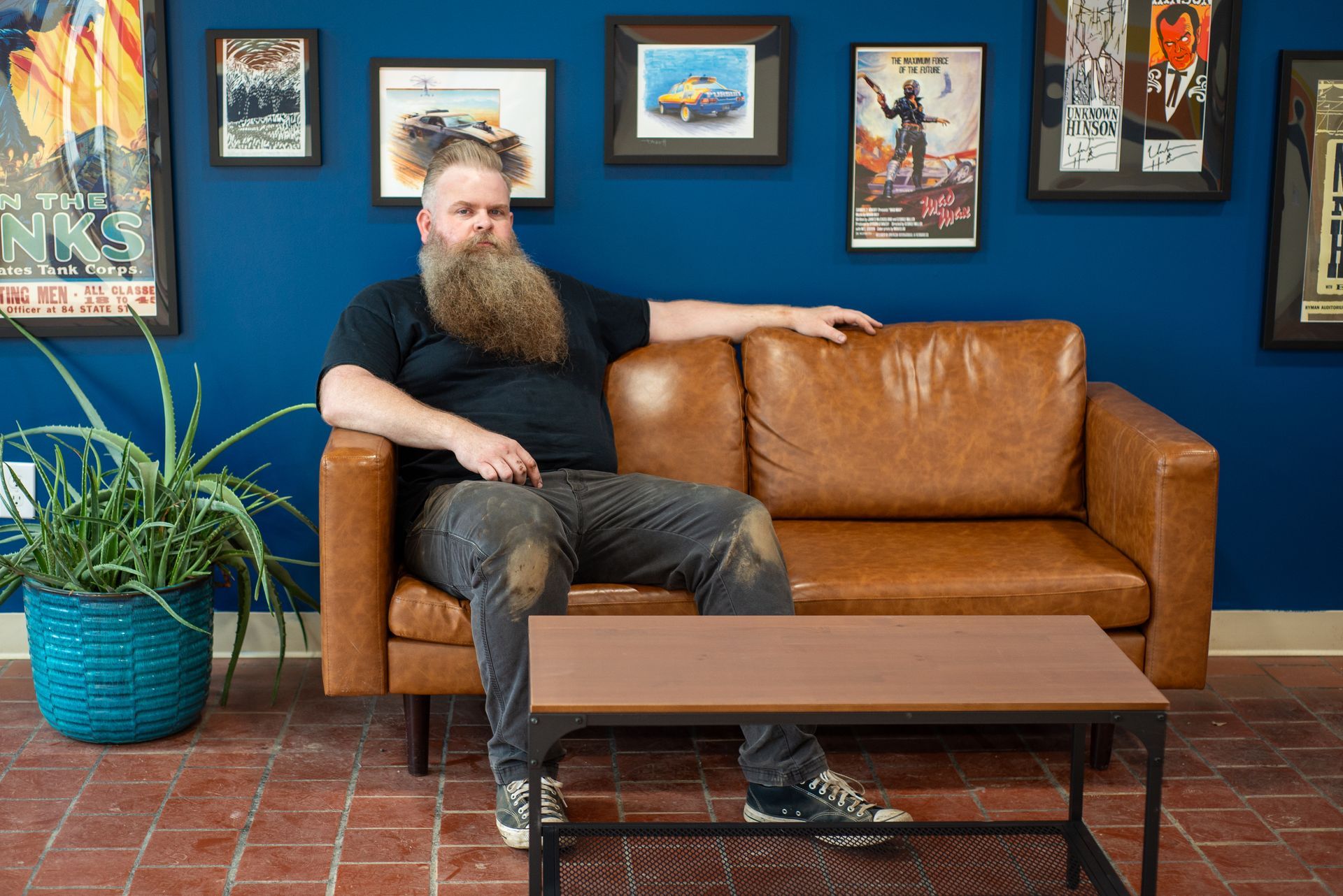 A man with a beard is sitting on a brown leather couch. | Top Auto Repair
