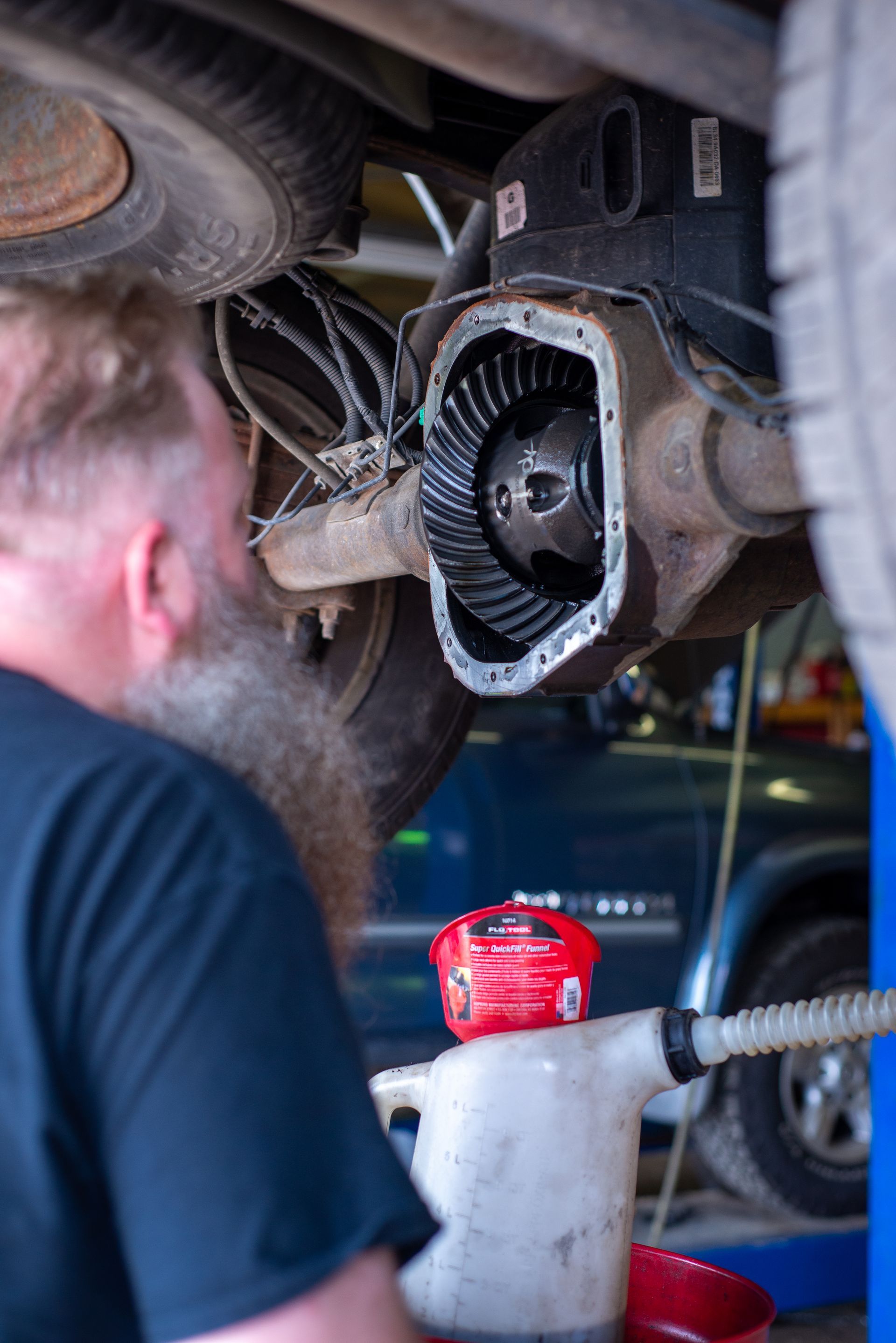 A man with a beard is working on the underside of a truck.