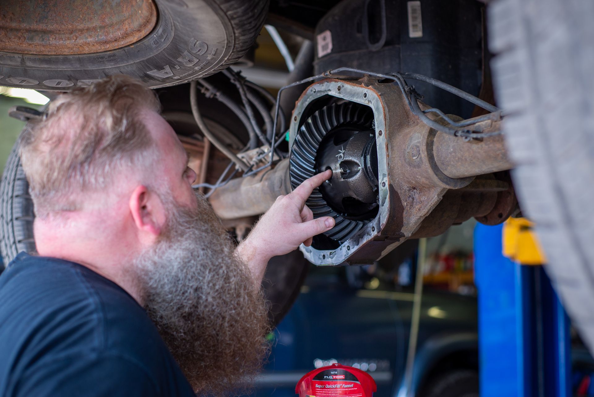 A man with a beard is working on the underside of a truck.