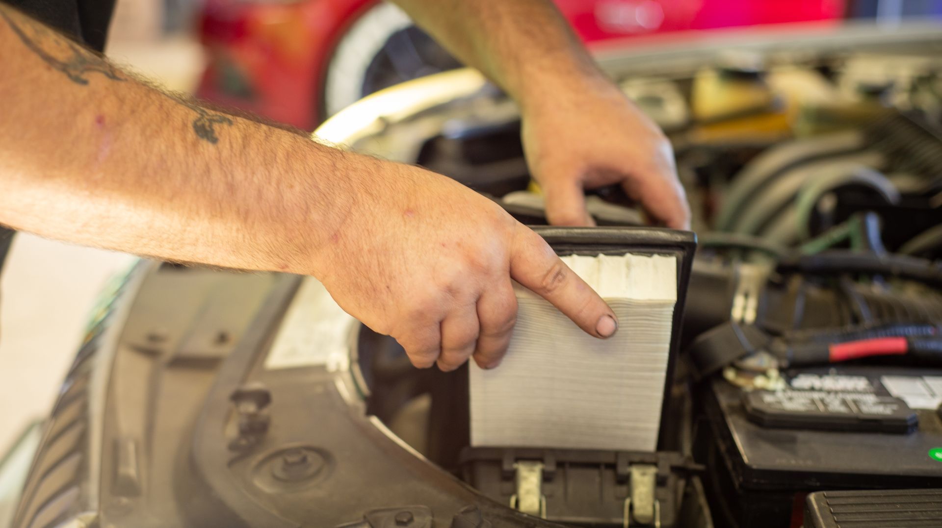 A man is pointing at a piece of paper in the engine compartment of a car.