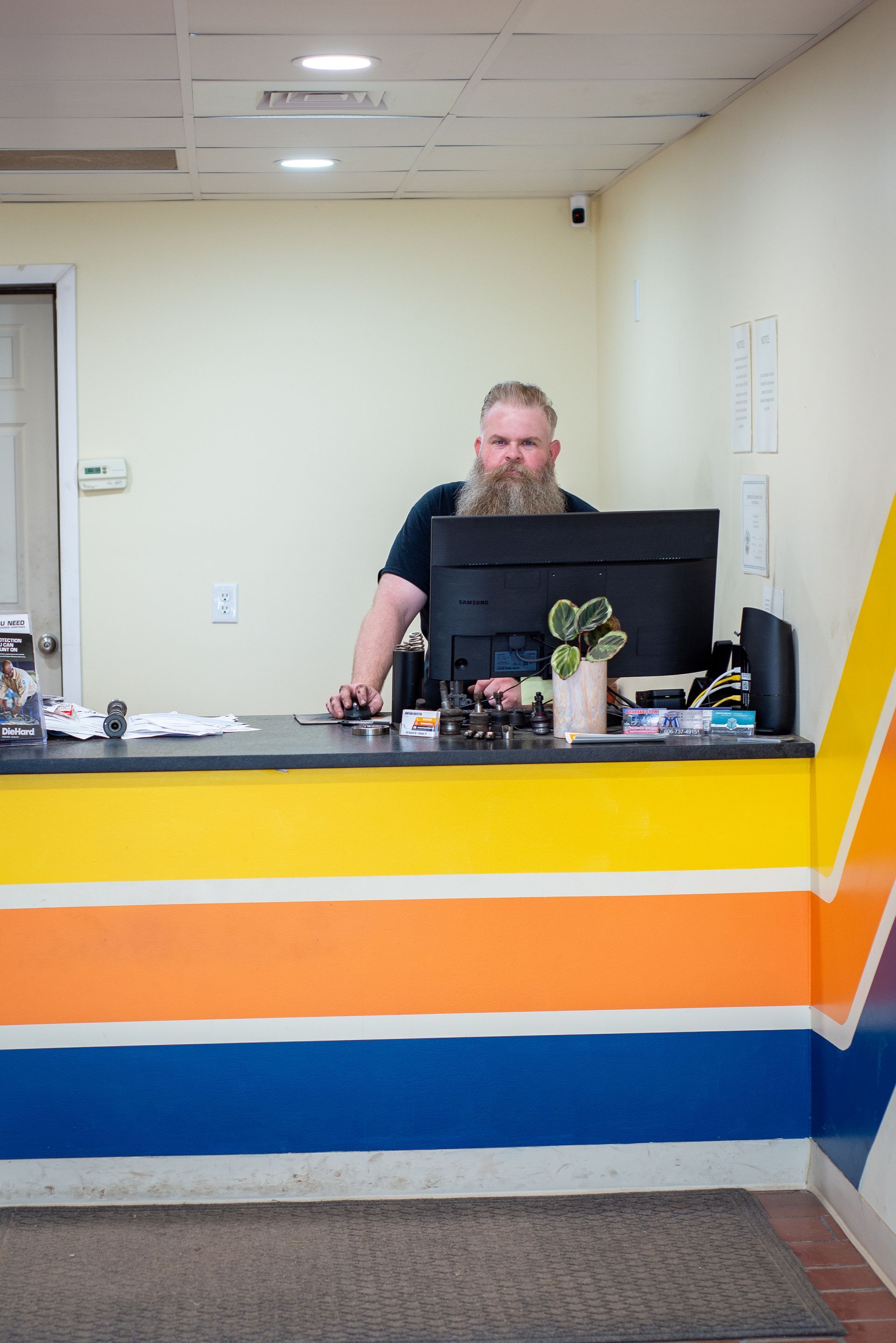 A man with a beard is standing at a counter in front of a computer. | Top Auto Repair