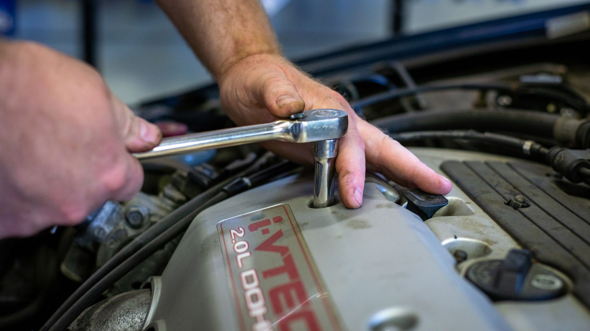 A man is working on a car engine with a wrench. | Top Auto Repair