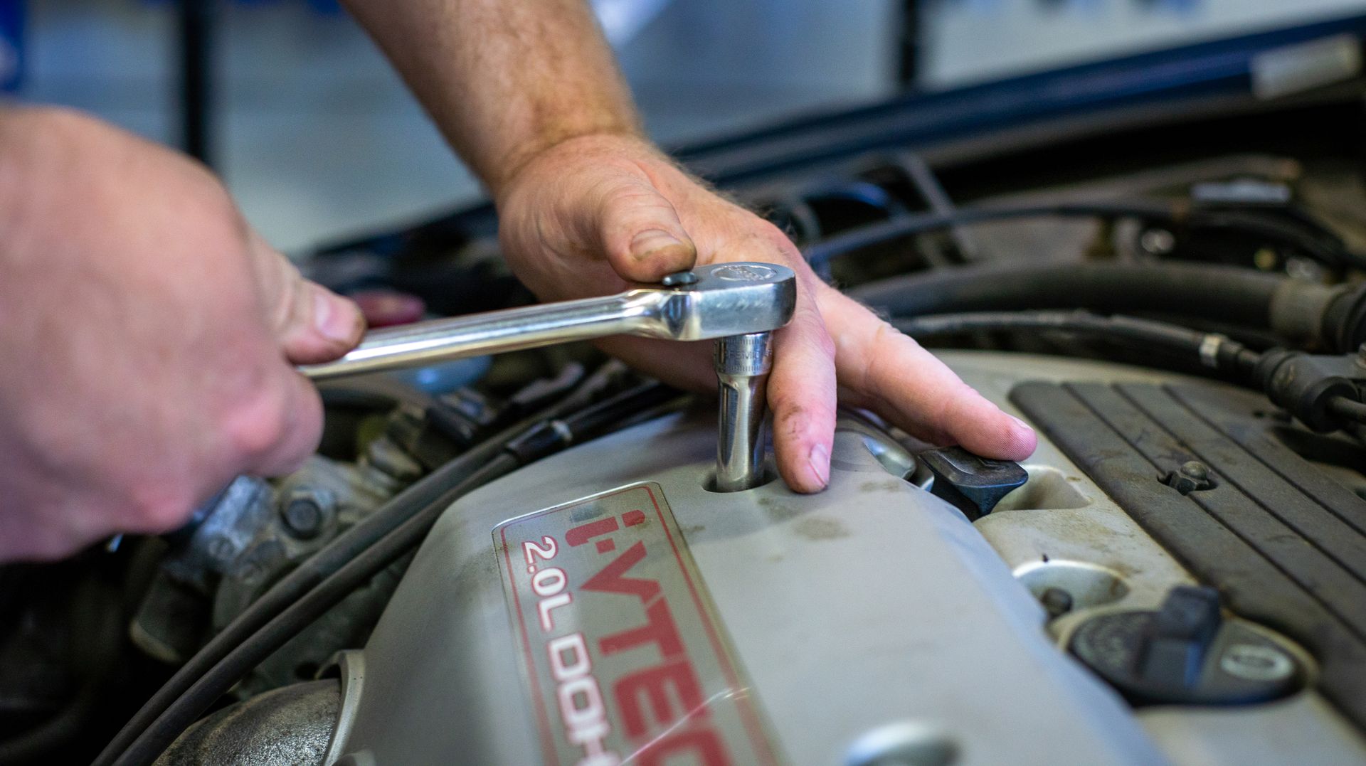 A person is working on a car engine with a wrench. | Top Auto Repair