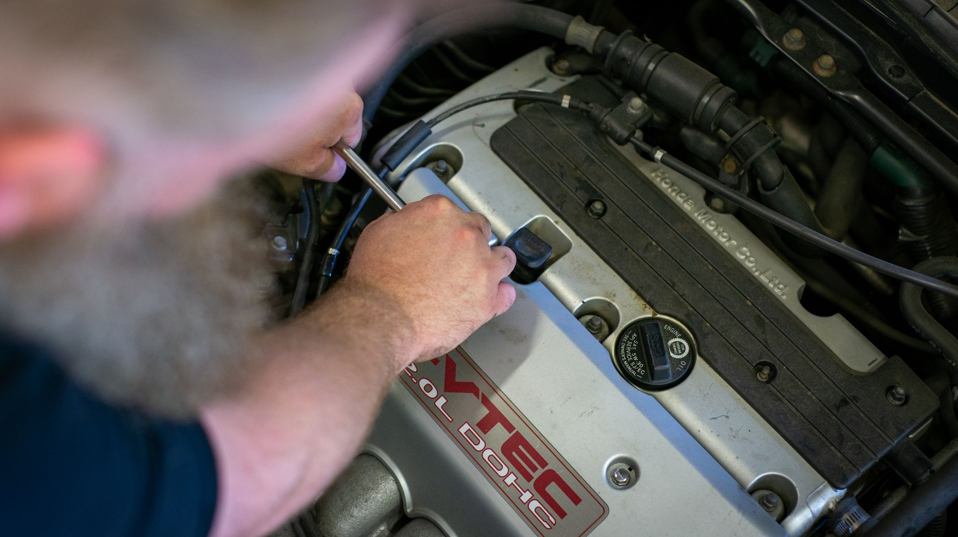 A man is working on a car engine with a screwdriver. | Top Auto Repair