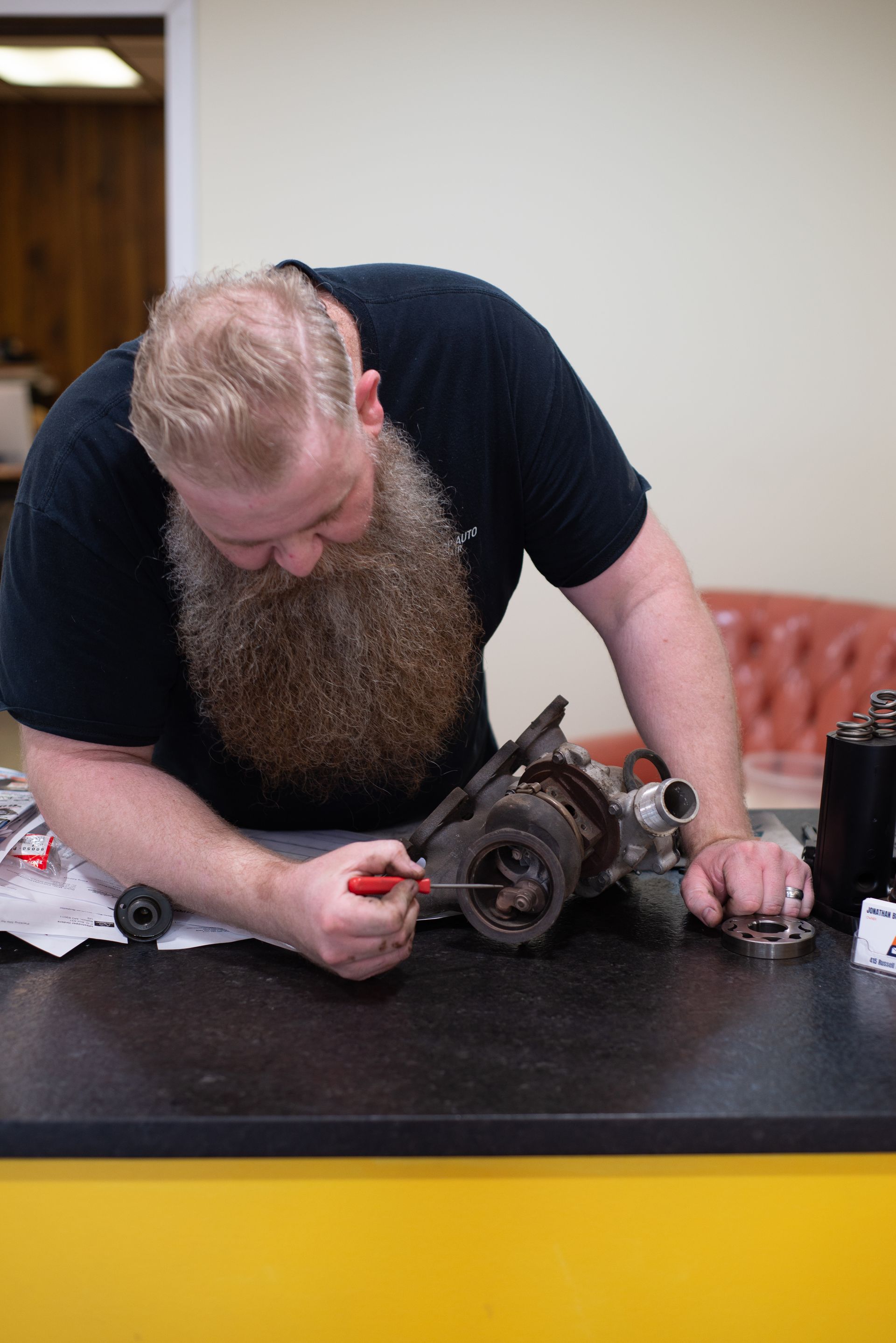 A man with a beard is working on a piece of equipment on a table. | Top Auto Repair