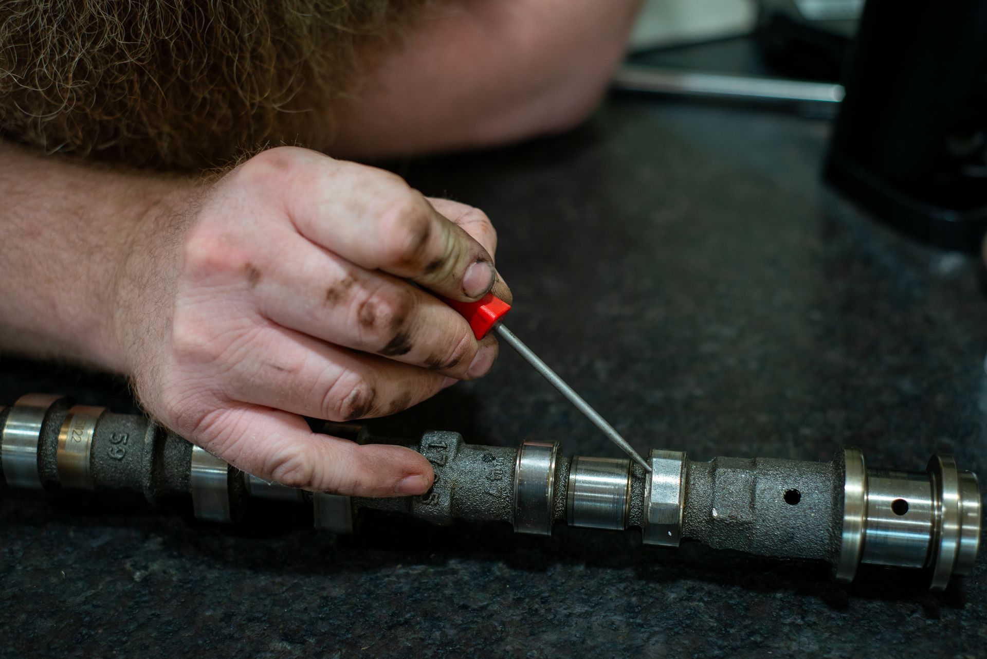 A man is working on a camshaft with a screwdriver. | Top Auto Repair