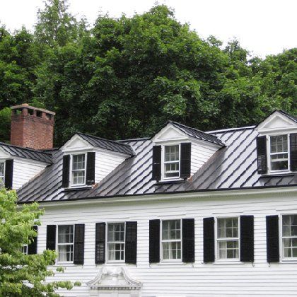 A white house with black shutters and a metal roof