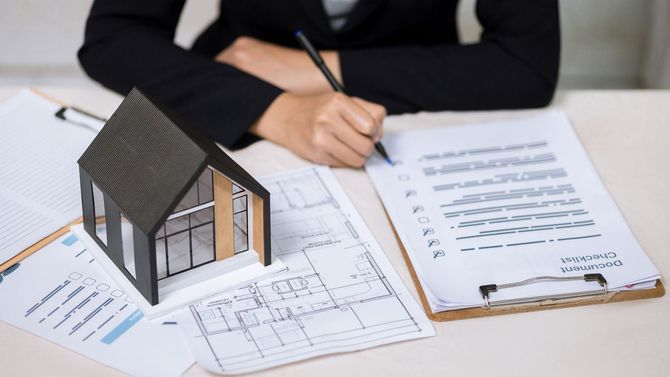 Architect reviewing house plans and signing documents beside a small house model