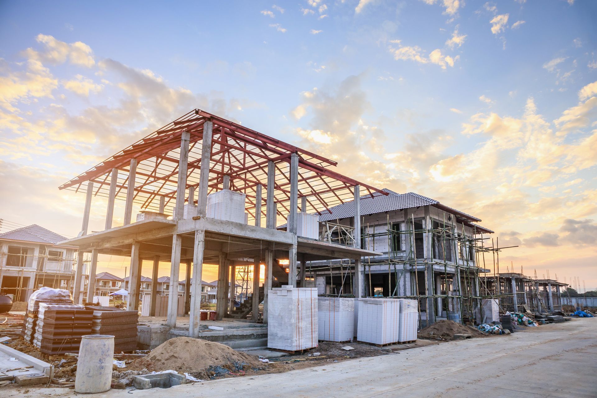 Partially built two-story house under construction at sunset, with framing, scaffolding, and construction materials.