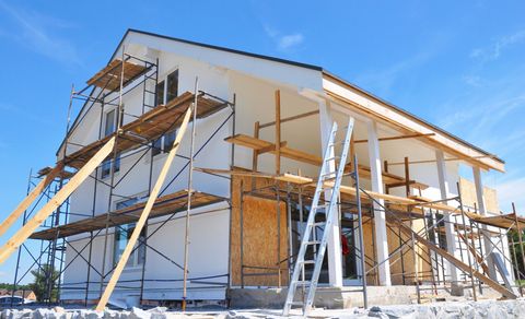 Two-story house under construction with scaffolding against a bright blue sky.