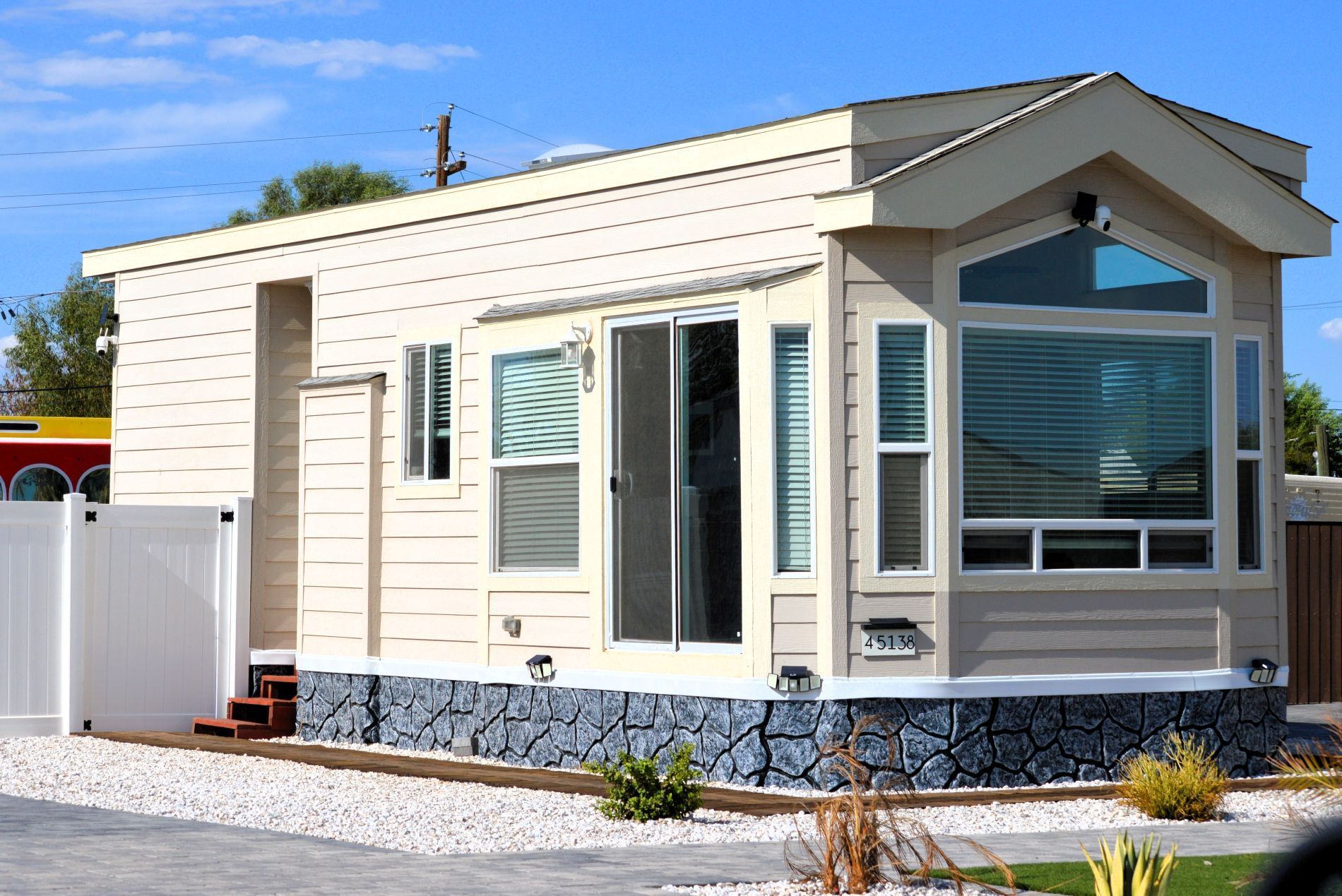 Beige manufactured home with stone base, large windows, and white fence.