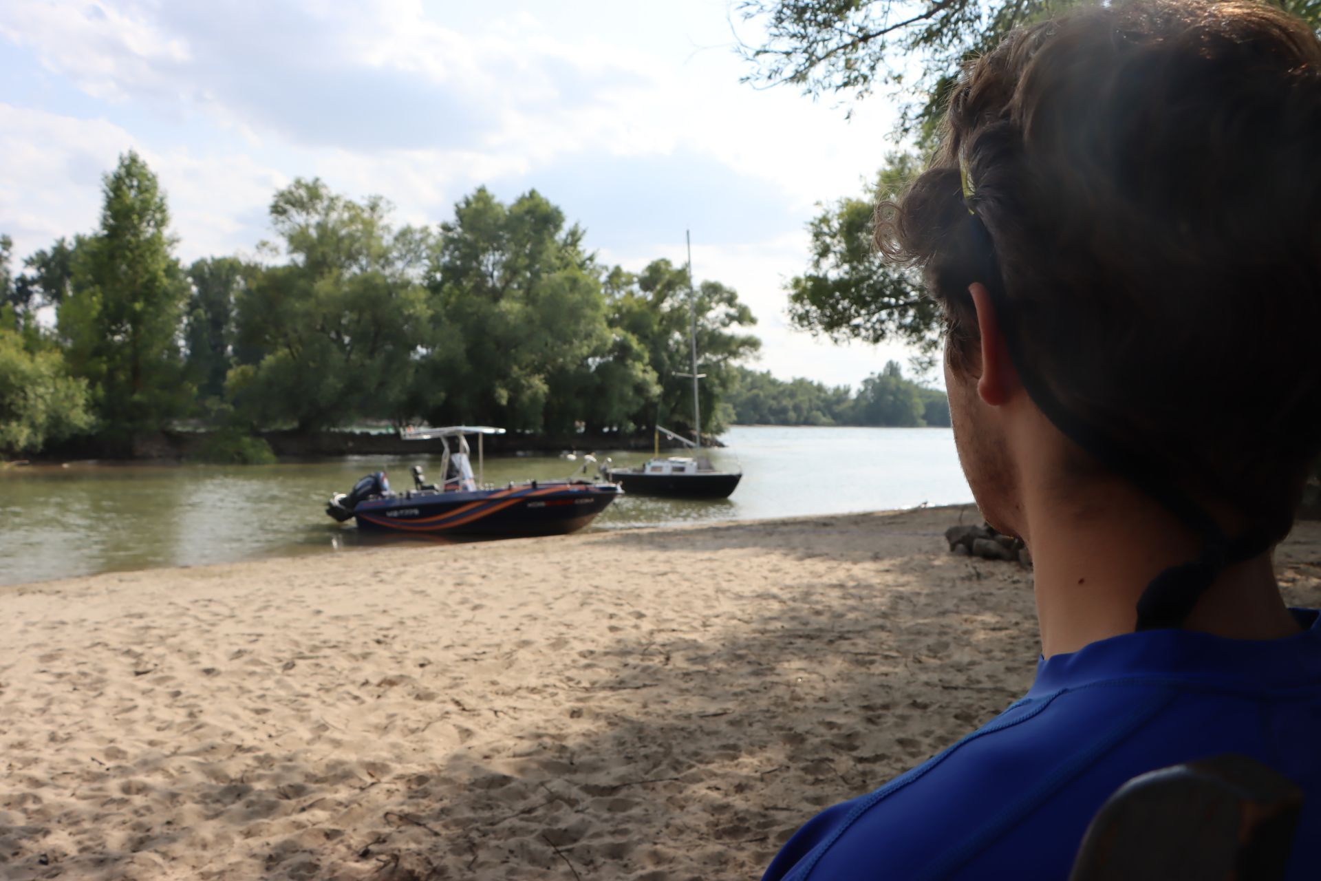 Ein Mann sitzt an einem Strand und schaut auf die Boote im Wasser