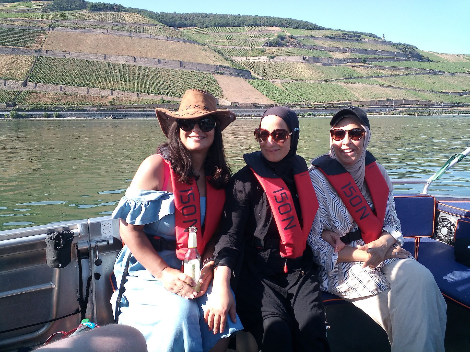 Drei Frauen sitzen auf einem Boot und tragen Schwimmwesten mit der Aufschrift „Rescue“ (Rettung)