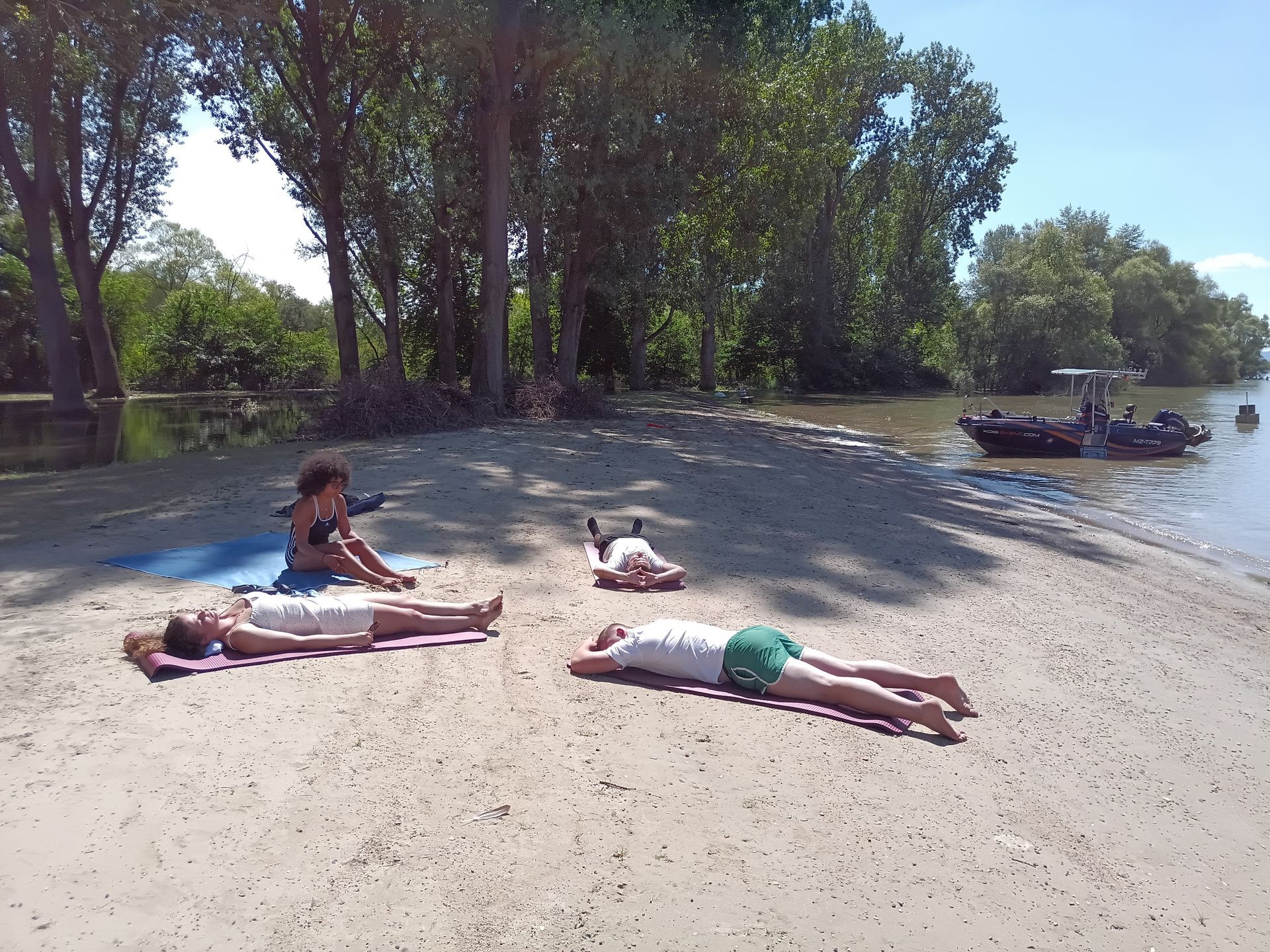 Drei Personen liegen an einem Sandstrand in der Nähe eines Gewässers