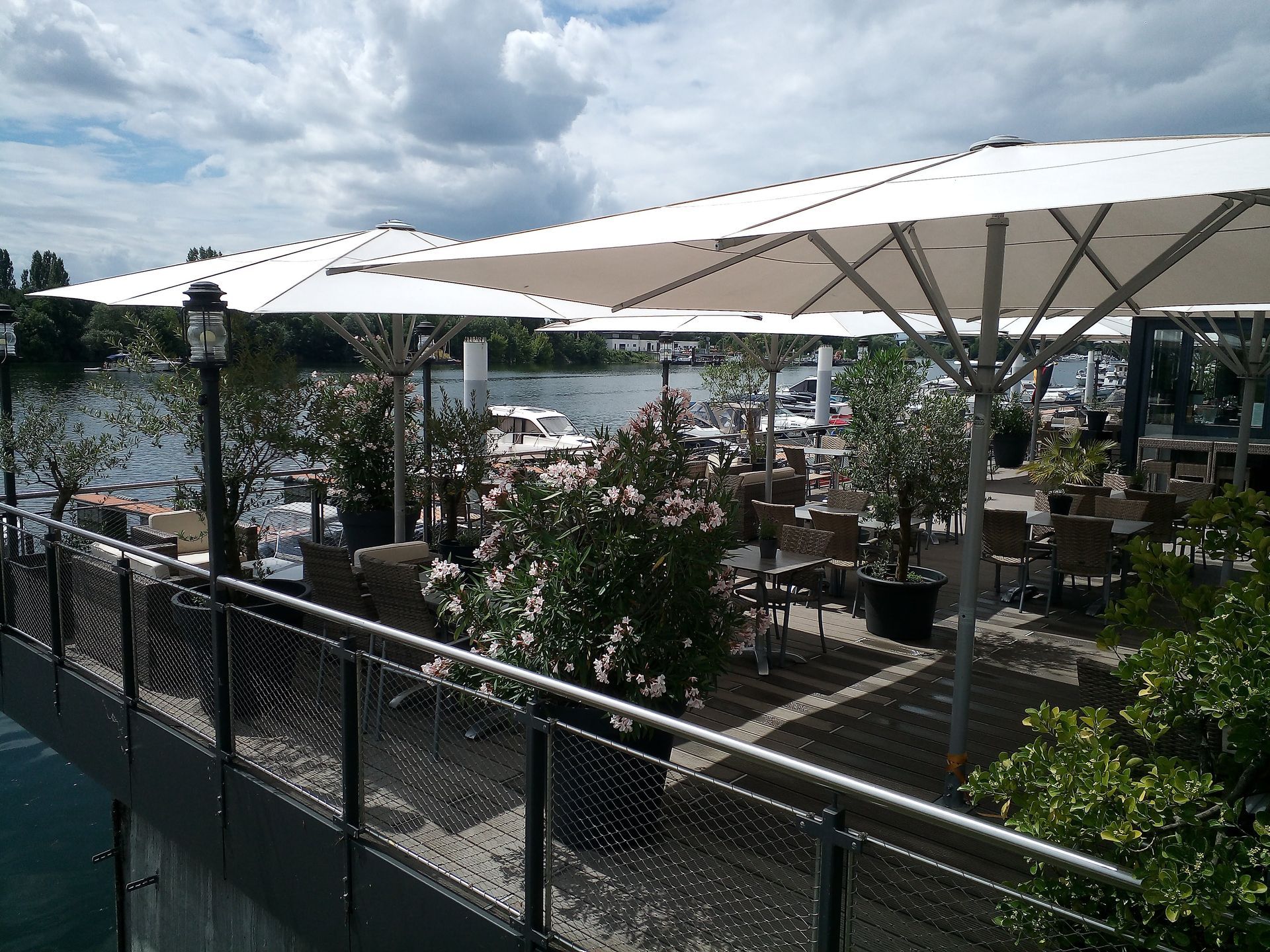 Eine Terrasse mit Tischen, Stühlen und Sonnenschirmen mit Blick auf ein Gewässer.