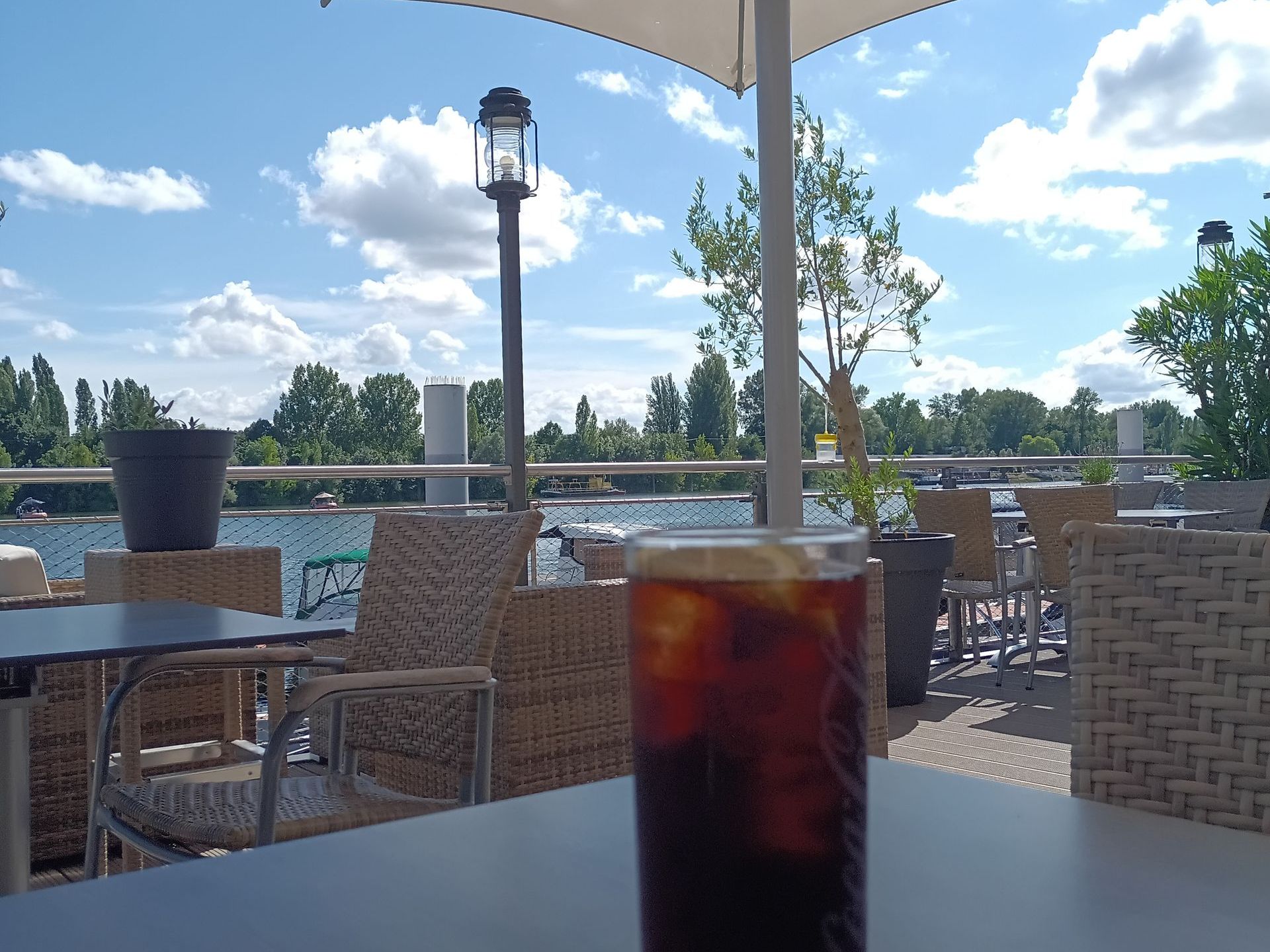 Ein Glas Cola steht auf einem Tisch vor einem See