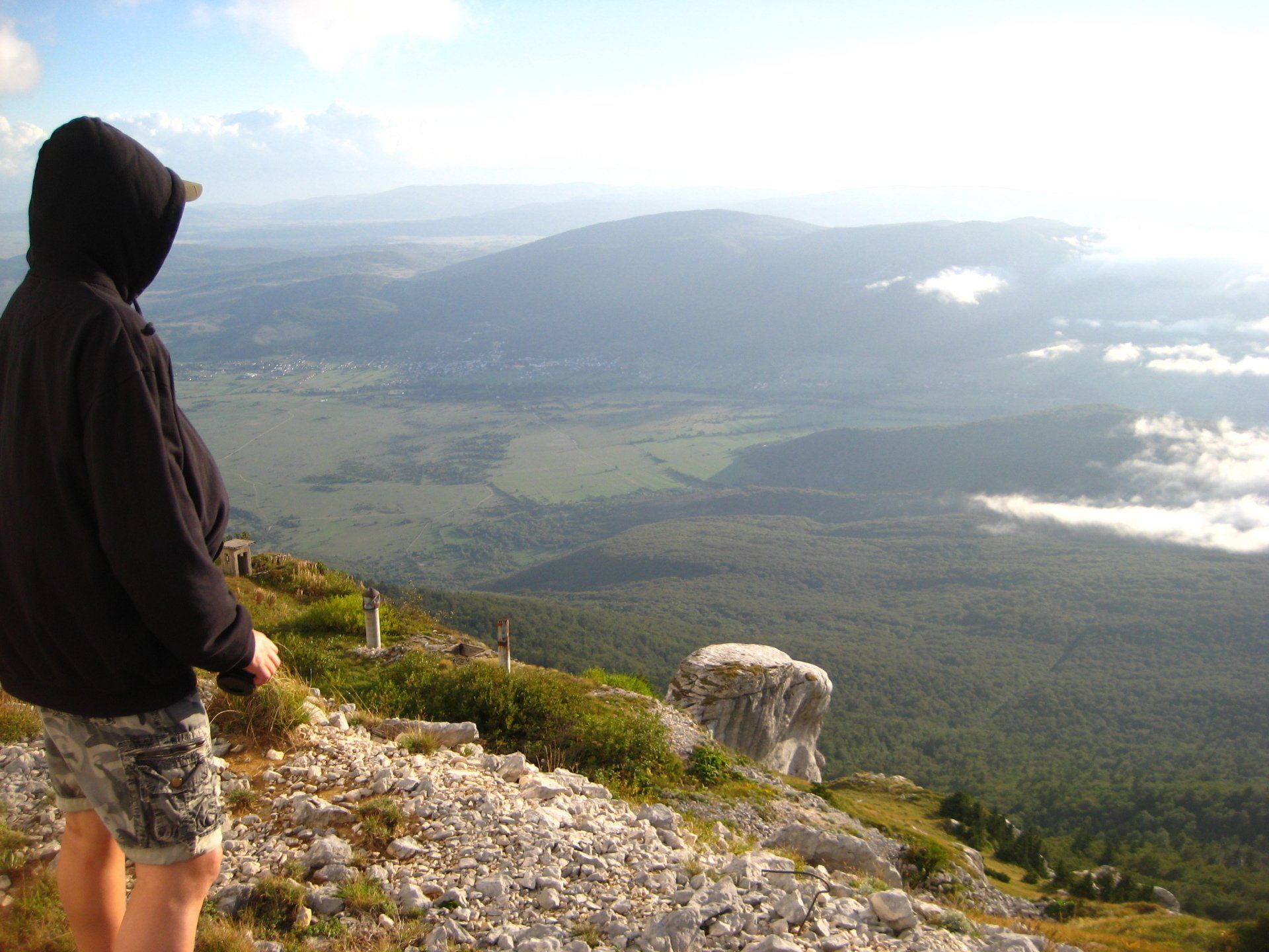 Eine Person in einer Kapuzenjacke steht auf einem felsigen Hügel mit Blick auf ein Tal