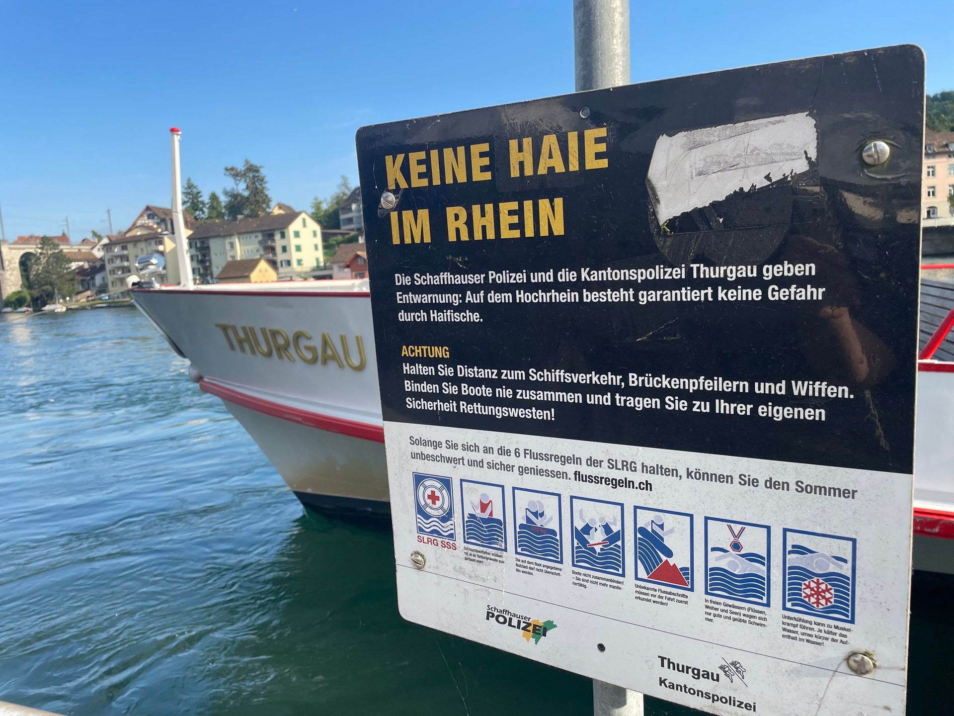 Ein Boot liegt neben einem Schild mit der Aufschrift „Keine Haie im Rhein“