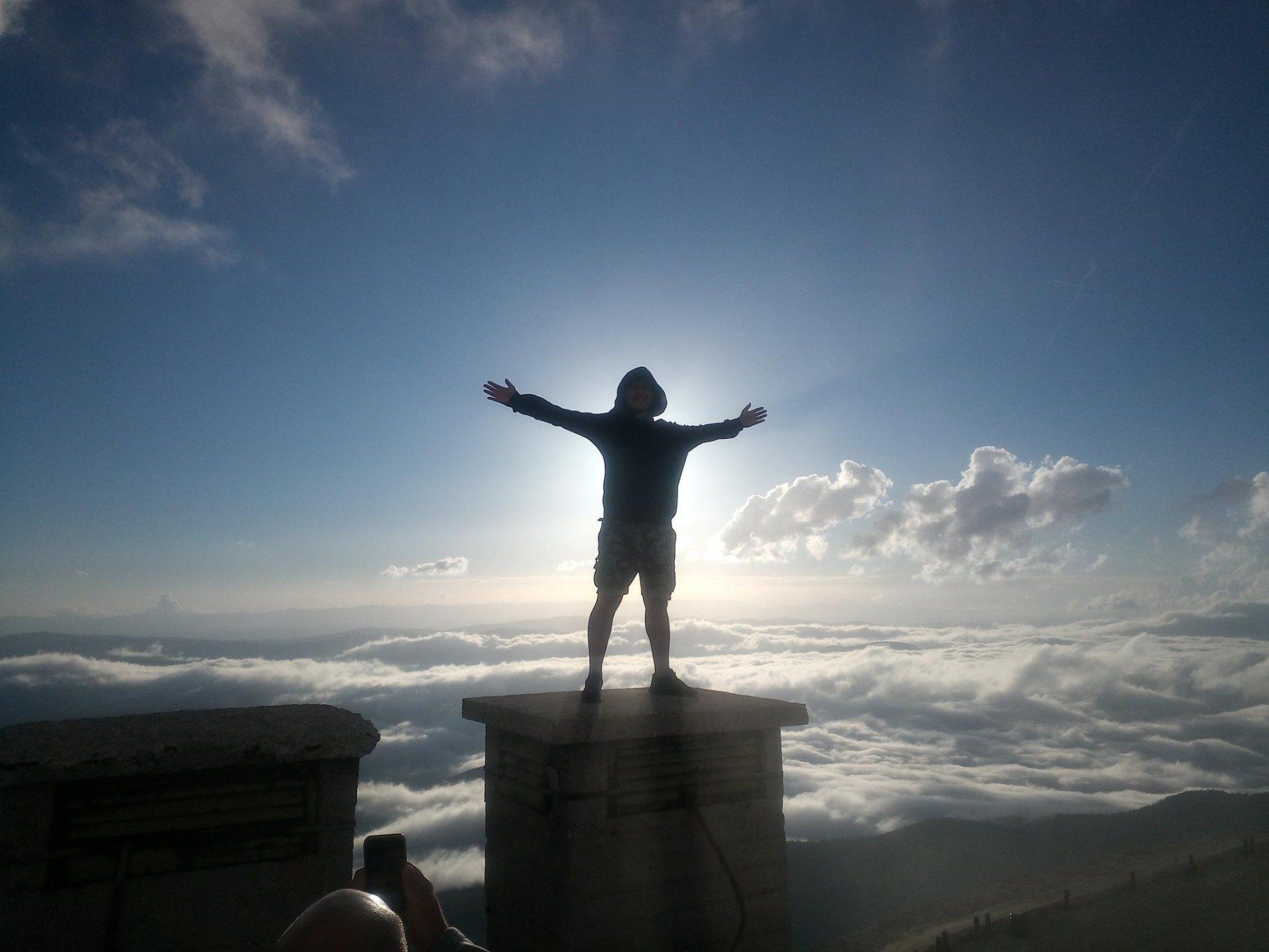 Eine Person mit ausgestreckten Armen, die auf einem wolkigen Berg steht