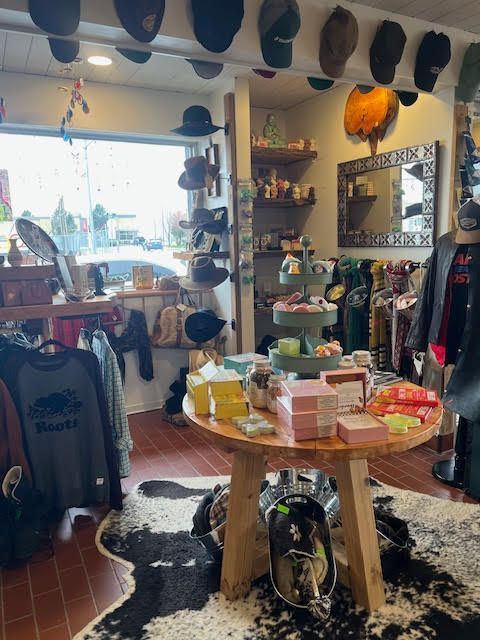 A boutique store interior with hats lining the ceiling, a round wooden table displaying merchandise, and a cowhide rug.
