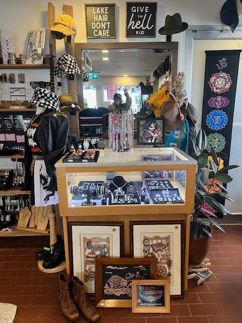 A store display counter with jewelry, hats, decor, and framed art in a retail shop.