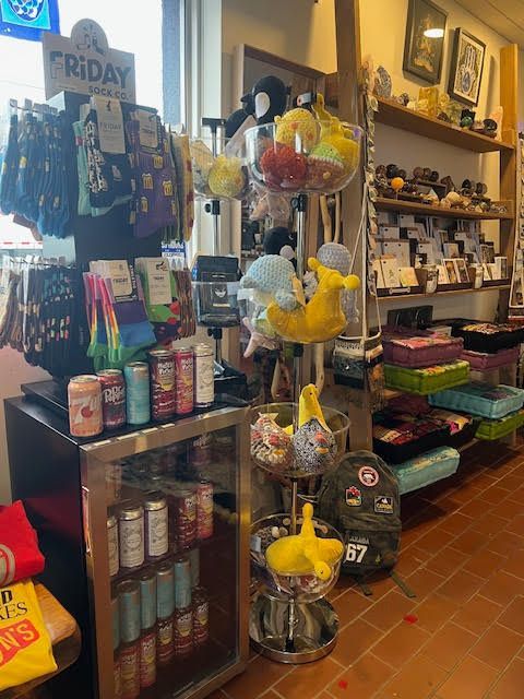 A store display featuring socks on a rack, canned drinks in a small fridge, and plush toys on a rotating stand.