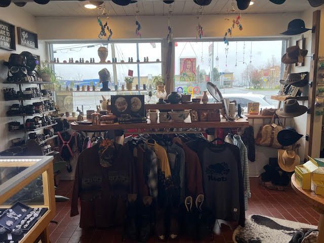 A retail shop interior displaying racks of clothing, various hats on shelves and walls, and shelves with small accessories.