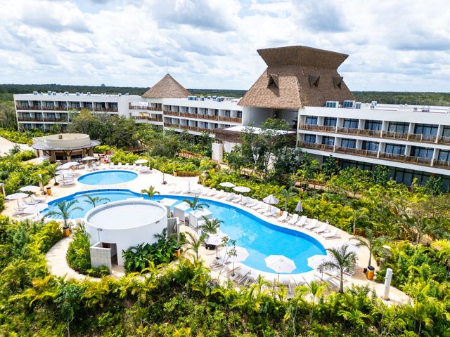Vista aérea de un complejo turístico tropical con piscinas azules serpenteantes, edificios blancos y exuberante vegetación.