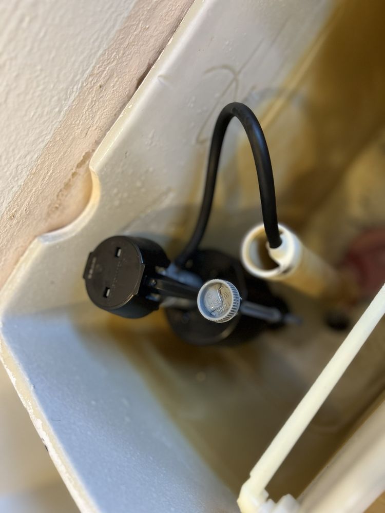 A close up of a toilet tank with a black hose attached to it.
