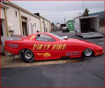 A red dirty bird race car is parked in front of a building