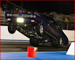 A purple car is doing a wheelie on a race track.