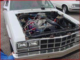 A white car with the hood open has a large engine inside