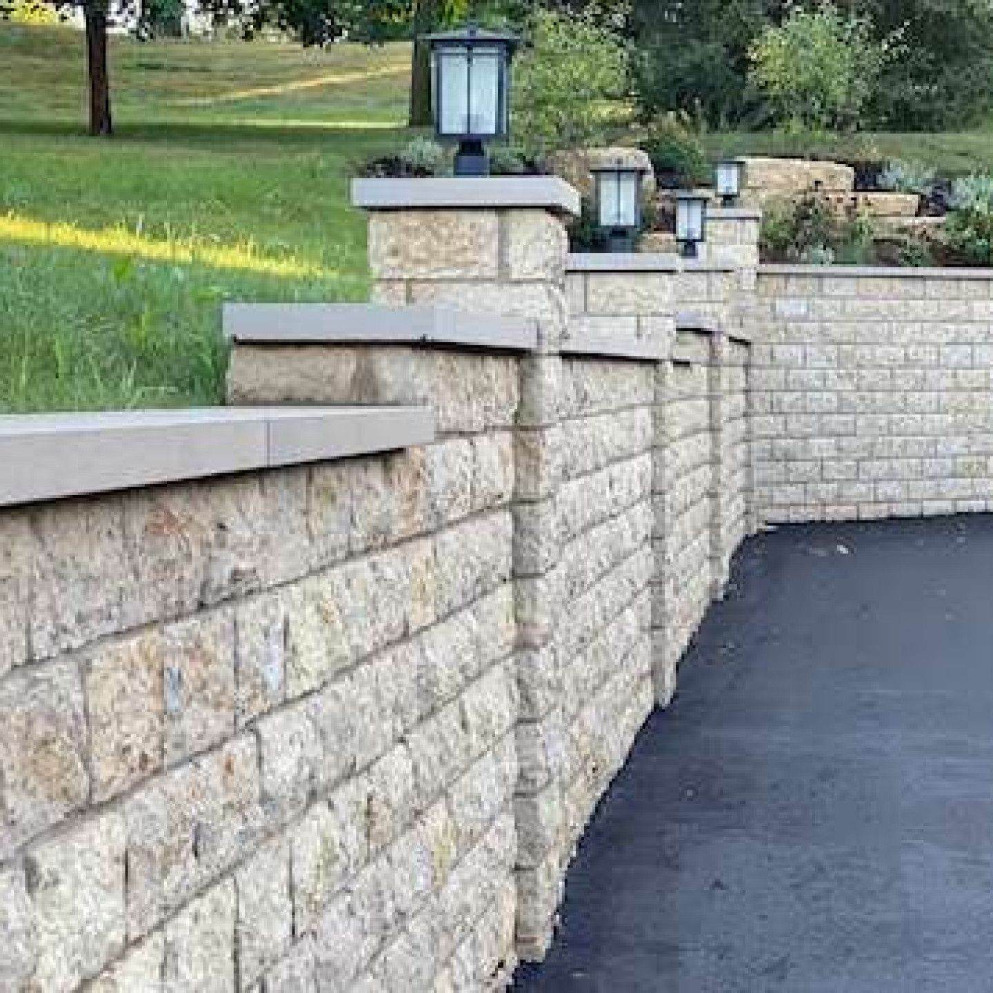 A brick wall with lanterns on top of it and a grassy hill in the background.