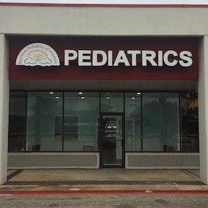 Pediatrics clinic storefront with large white sign on a maroon awning and glass entrance doors