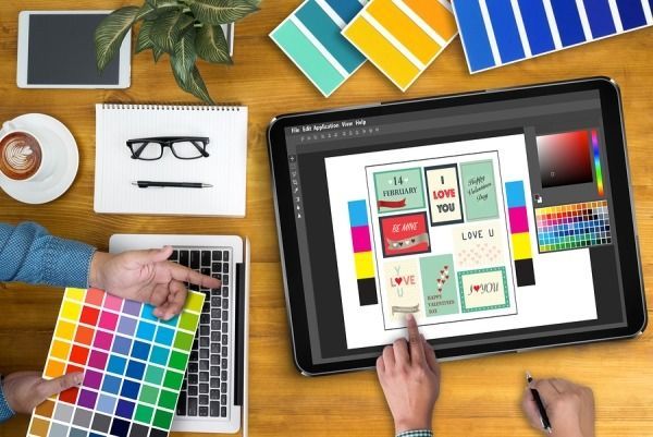 Graphic designer at work, showing color palette and using tablet to design greeting cards.