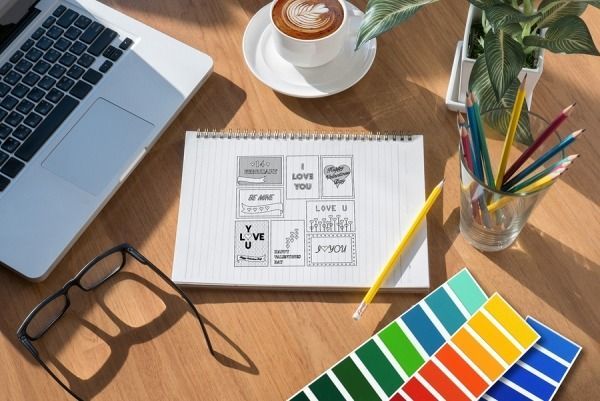 Desk with laptop, notebook, coffee, glasses, and color swatches; a graphic designer's workspace.