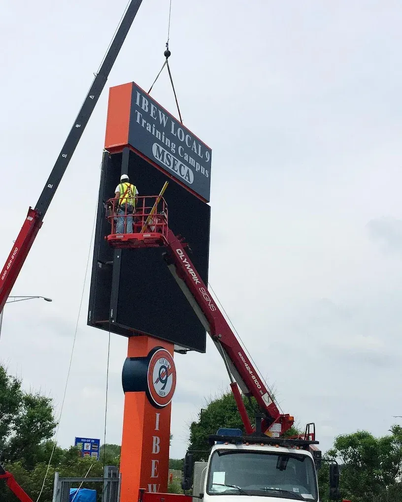 Construction crew installing a large digital sign for IBEW Local 4 Training Campus with crane and lift.