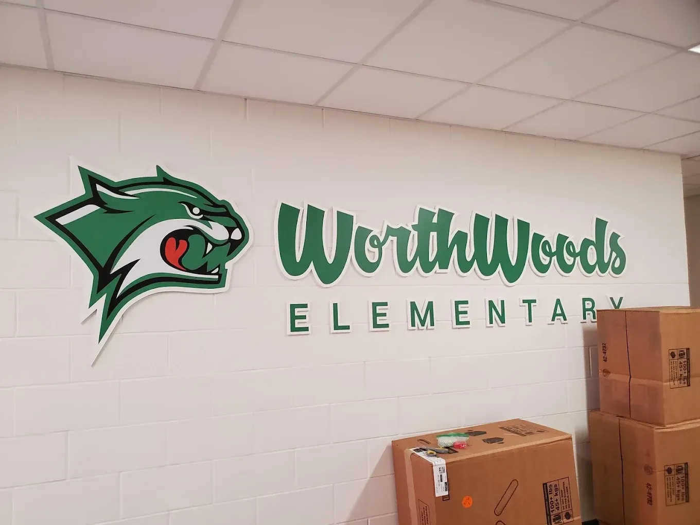 Worth Woods Elementary school sign with green panther logo on white wall.