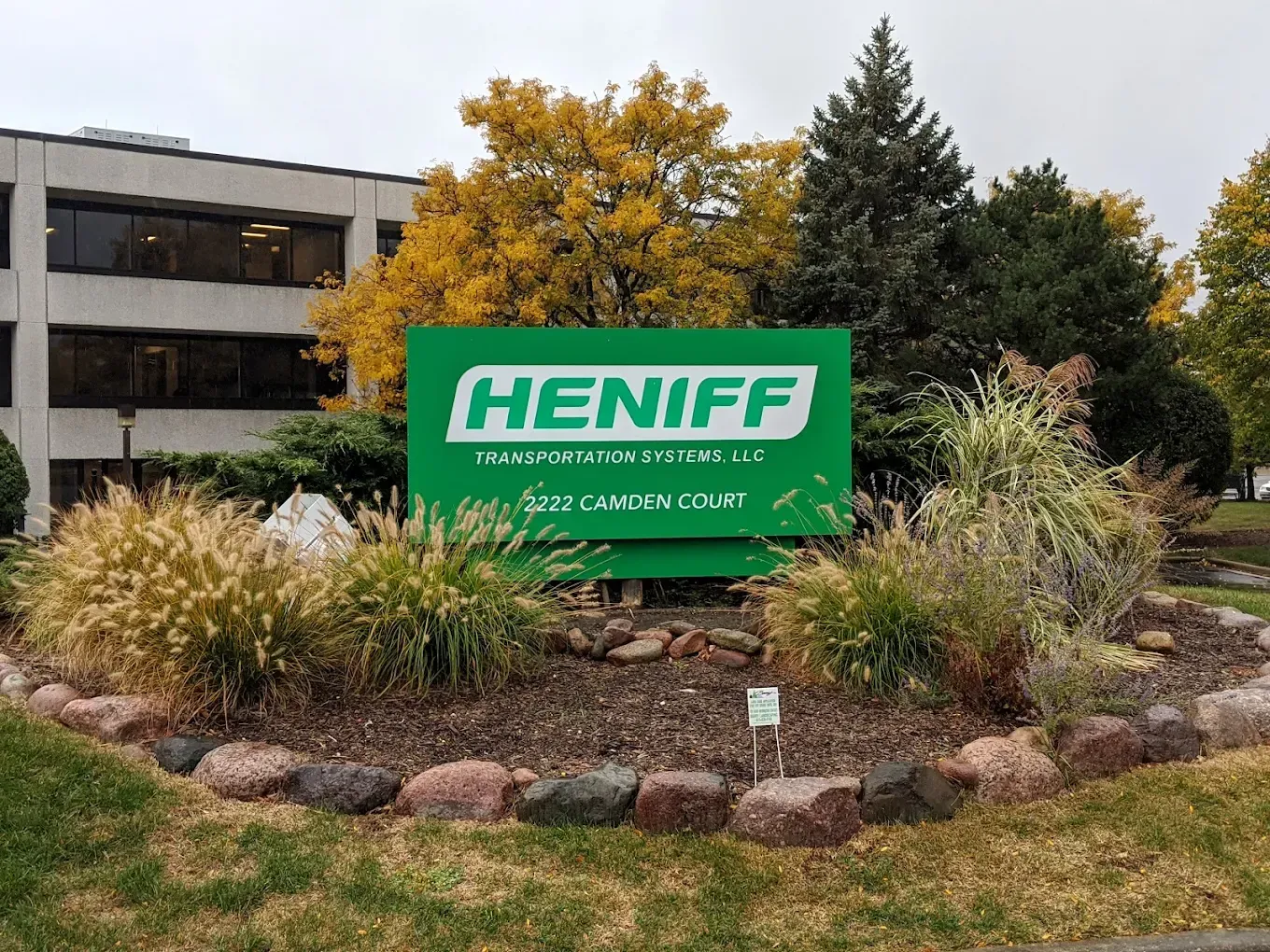 Green Heniff Transportation Systems sign in front of a building with fall foliage.