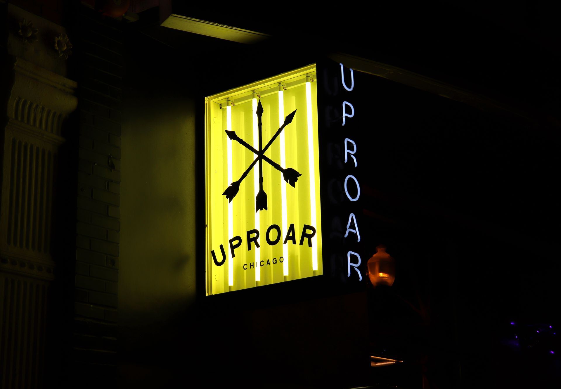 Neon sign for "Uproar" bar with an arrow symbol, lit up at night.
