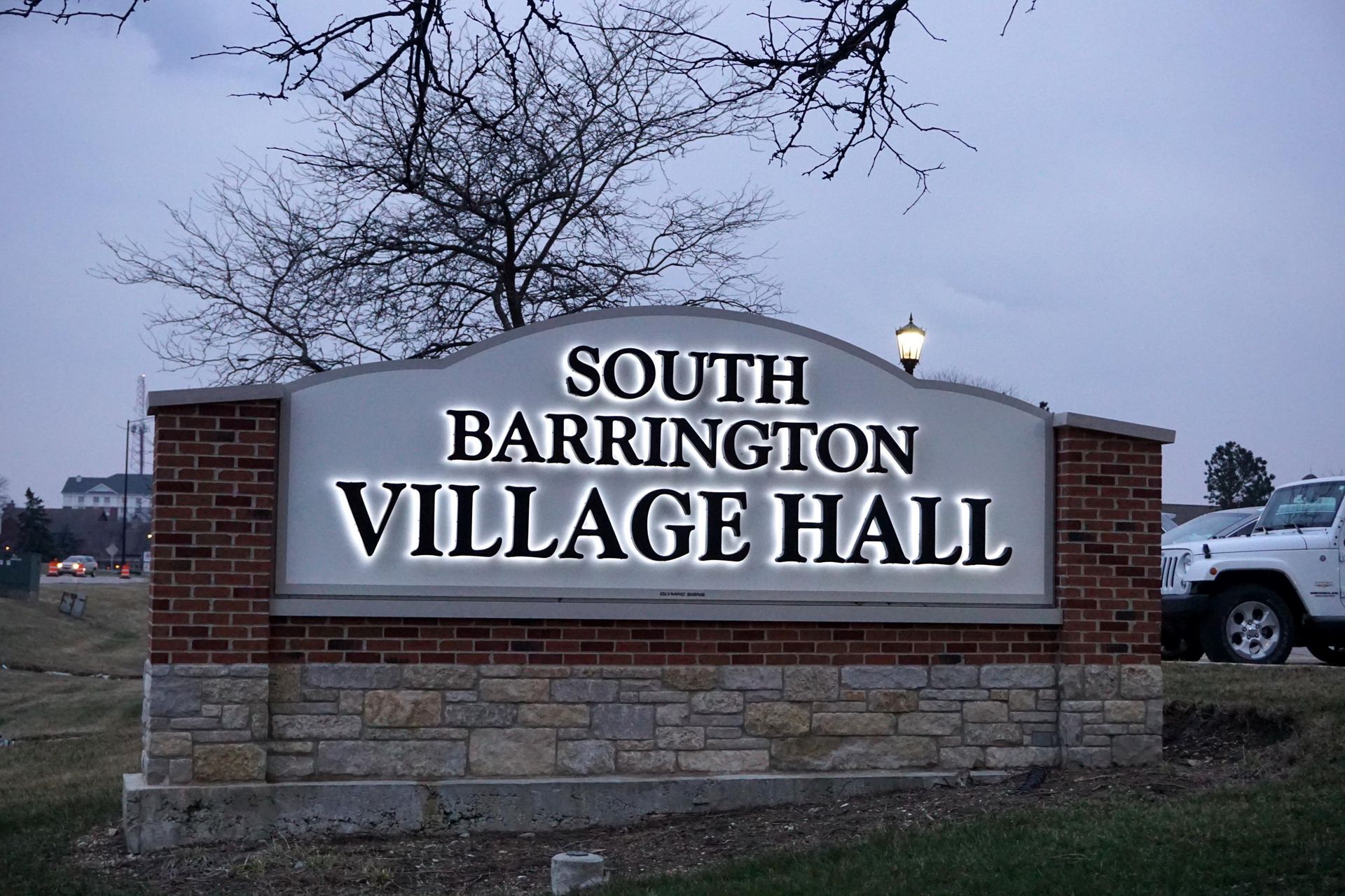 Sign for South Barrington Village Hall at dusk, with lit lettering, brick and stone facade.