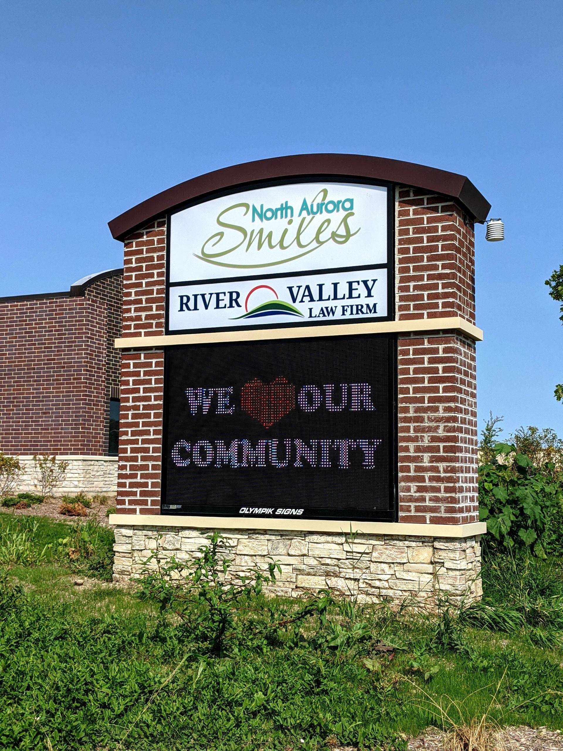 Sign for North Aurora Smiles dental office with electronic display; brick and stone structure.