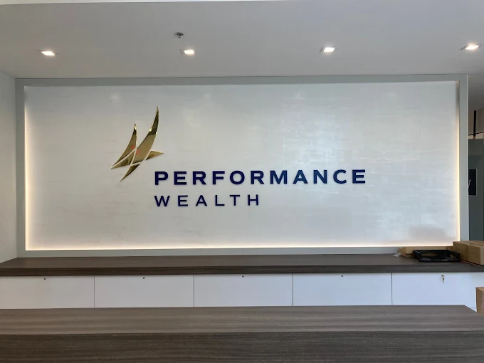 Sign for Performance Wealth with logo and text on a white wall above a counter.