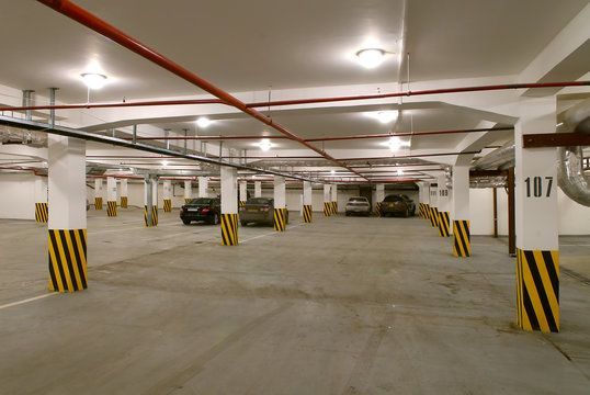 Indoor parking garage with cars, white pillars, yellow and black stripes.