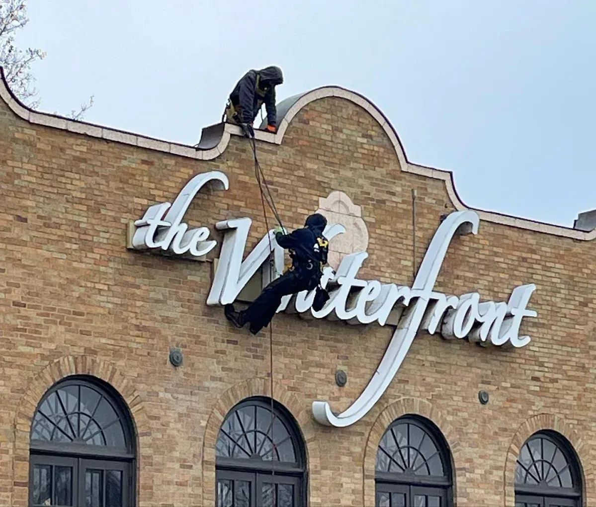 Two people, possibly police, on the roof of “The Waterfront” building; one rappels down, secured by a rope.