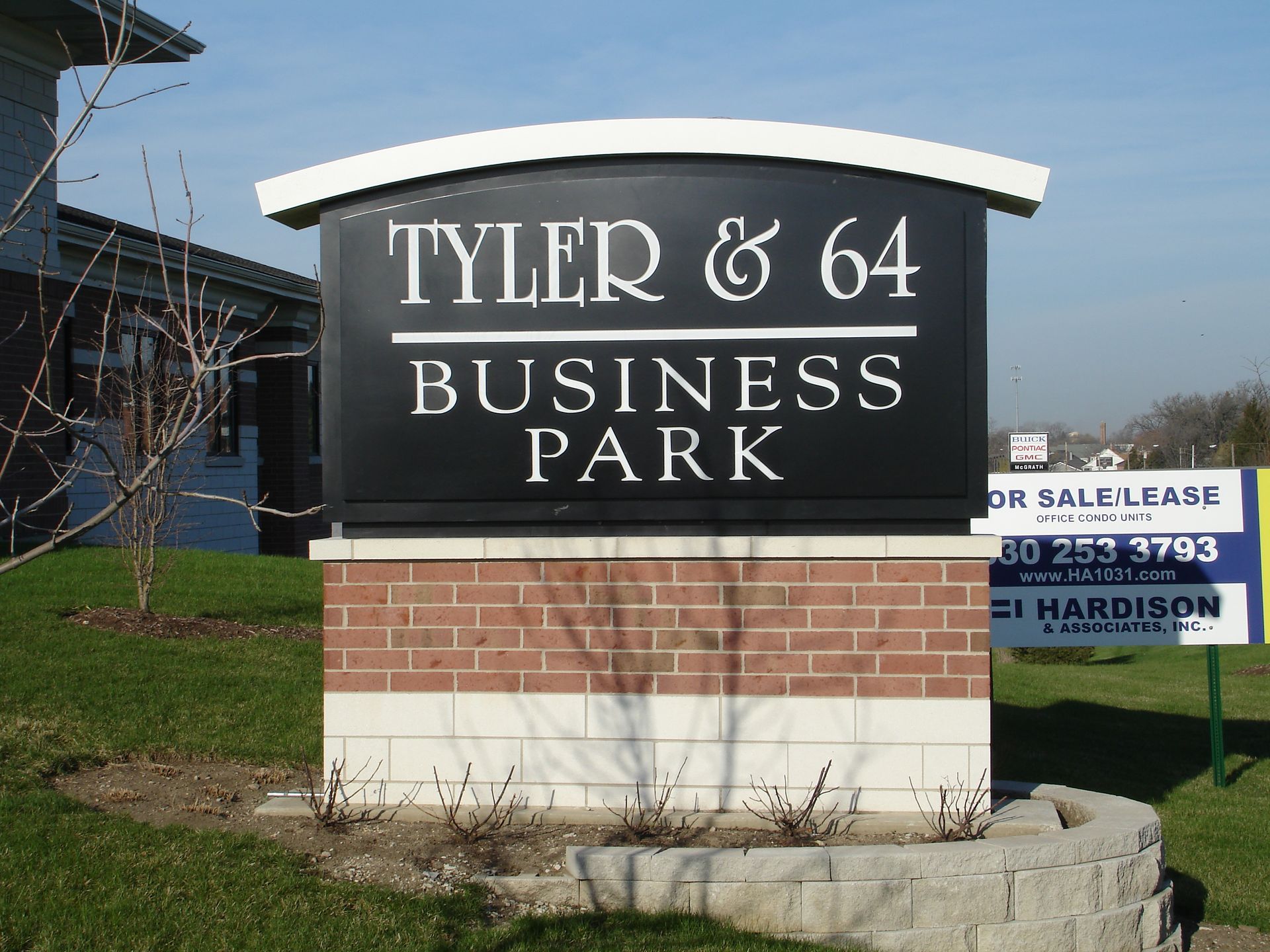 Sign for Tyler & 64 Business Park, black background, white lettering, brick base, and green grass.