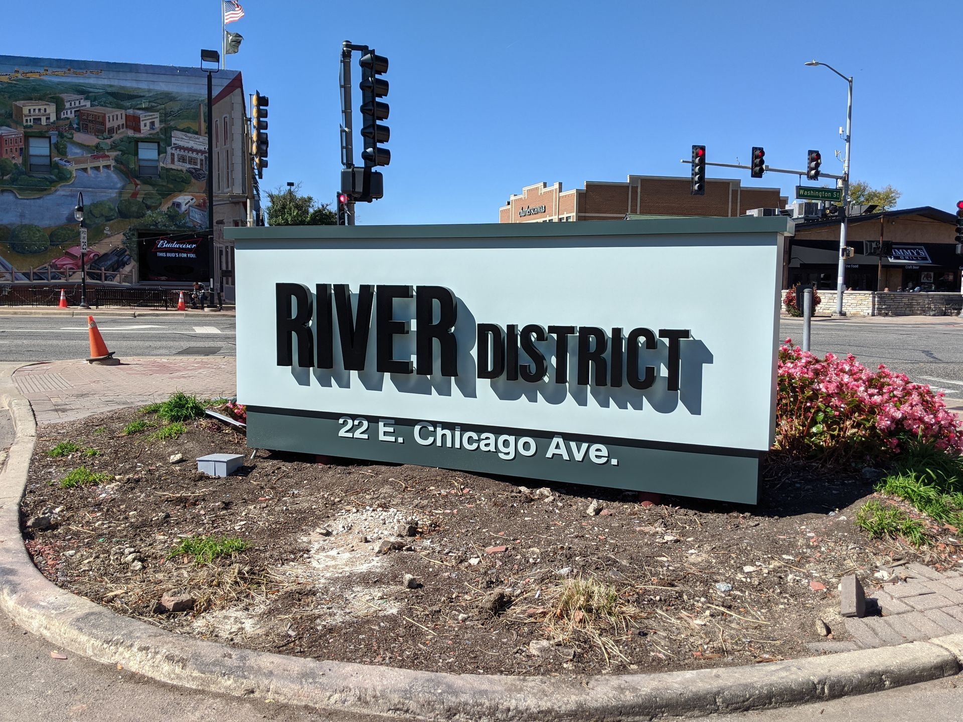 Sign for River District at 22 E. Chicago Ave. in front of a building, under a blue sky.