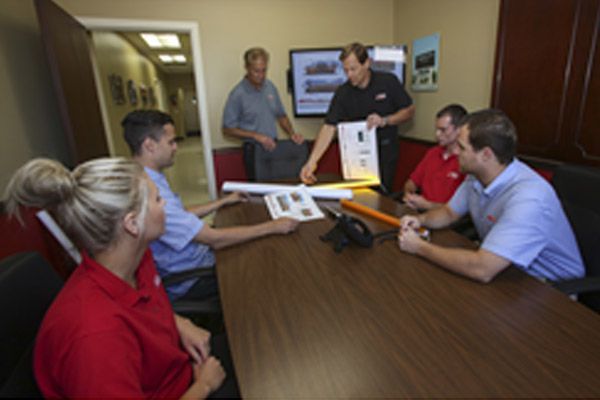 People in a meeting: men and woman at a table with a presentation.  A screen displays images.