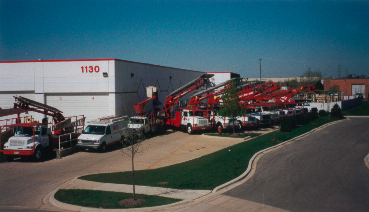 Red and white trucks with raised arms parked outside a white building with the number 1130.